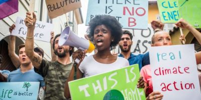 Someone with a megaphone surrounded by climate activists holding placards. Their signs read "it's our future," "real climate action" and "there is no planet B."