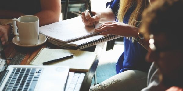 Woman writing in a notepad with group around desk