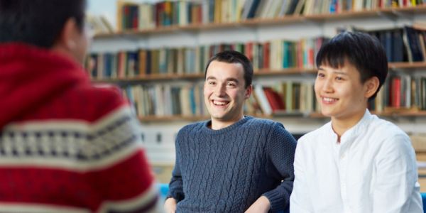Two students smiling at a person who is facing them in the foreground of the image